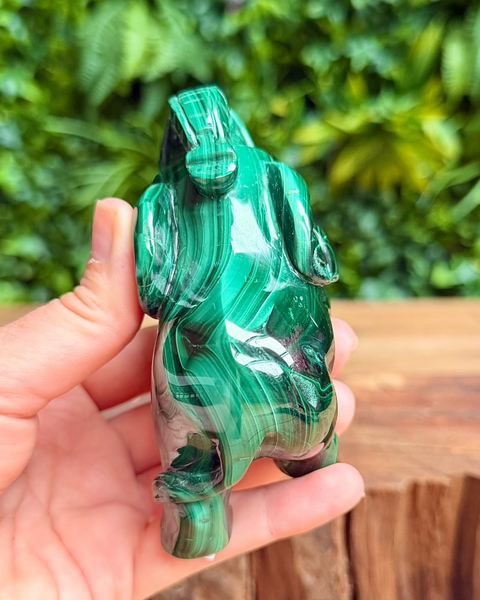 Green malachite elephant sculpture held in a hand with a blurred green foliage background