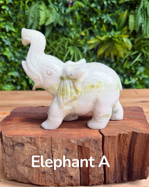 White jade elephant figurine on a wooden base with greenery in the background