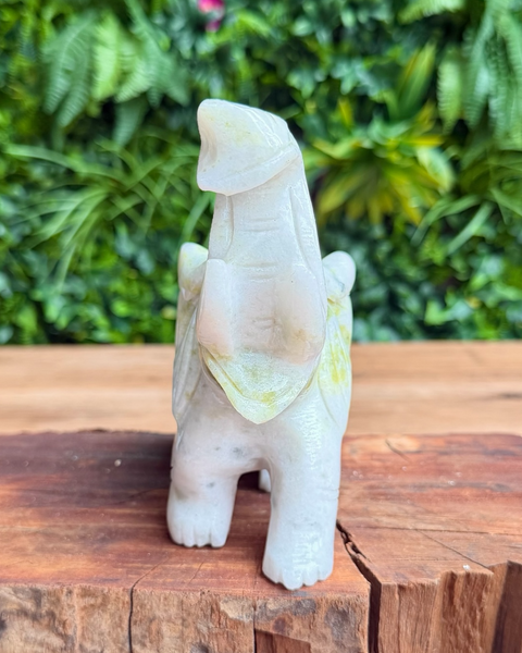 Carved crystal elephant on a wooden surface with green foliage in the background
