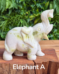 White jade serpentine elephant figurine on a wooden surface with greenery in the background