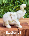 White crystal serpentine elephant figurine on a wooden surface with green foliage in the background