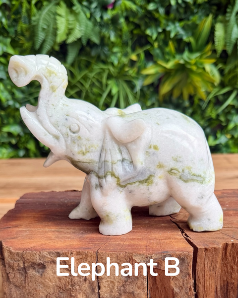 jade elephant carving on a wooden block with green foliage in the background