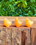 Three small orange chick figurines on a wooden surface with a green leafy background