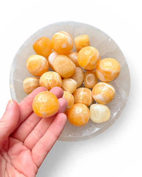Hand holding orange calcite tumble stone
