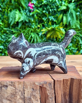 crystal cat figurine with white patterns on a wooden block with a green foliage background