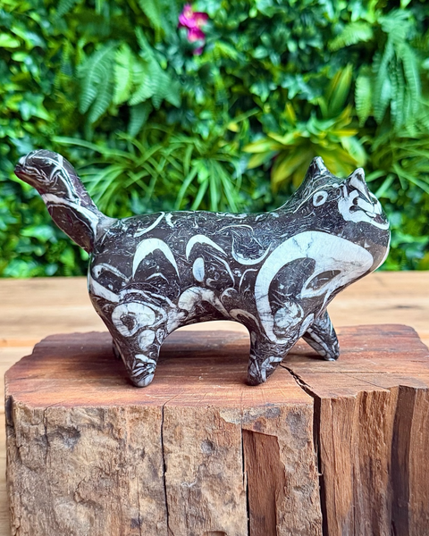Decorative cat-shaped stone sculpture on a wooden block with a green foliage background