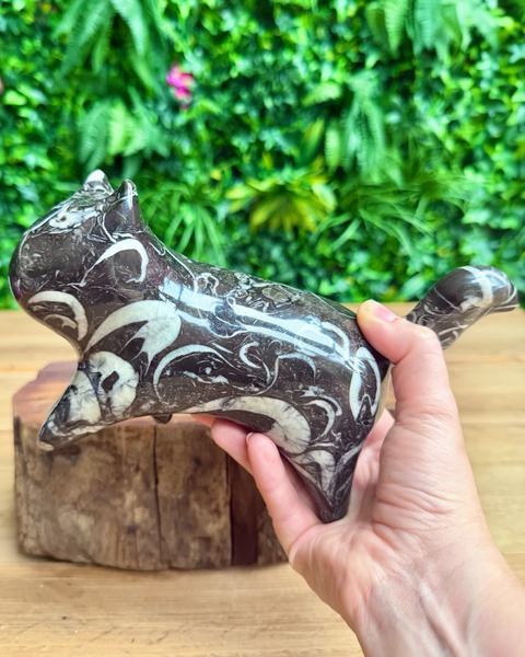 Marble-patterned sculpture of a cat held by a hand with a green foliage background