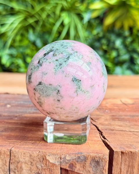 Pink and green crystal sphere on a wooden surface with a blurred green plant background