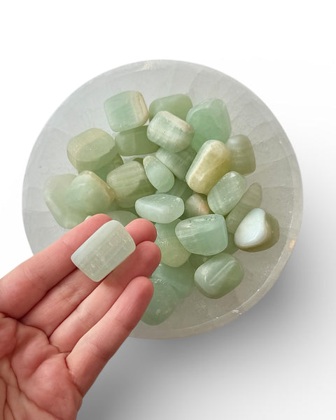 Hand holding a green pistachio calcite tumble stone
