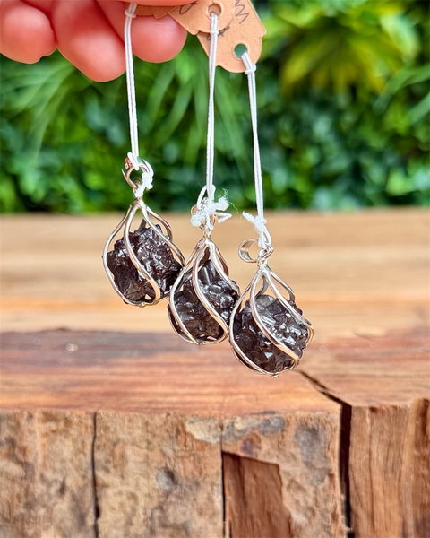 Silver pendants with dark prophecy stones on a wooden surface with greenery in the background