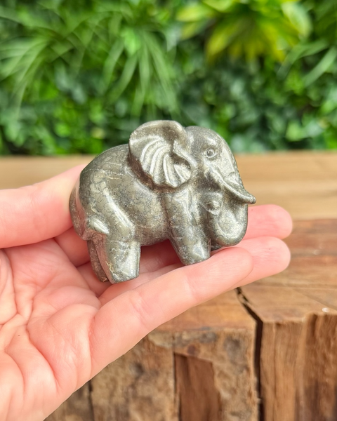 Small pyrite elephant figurine held in a hand with a blurred green background