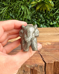 Hand holding a small metallic animal figurine against a natural background
