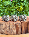 Three small pyrite elephant figurines on a wooden block with a natural background