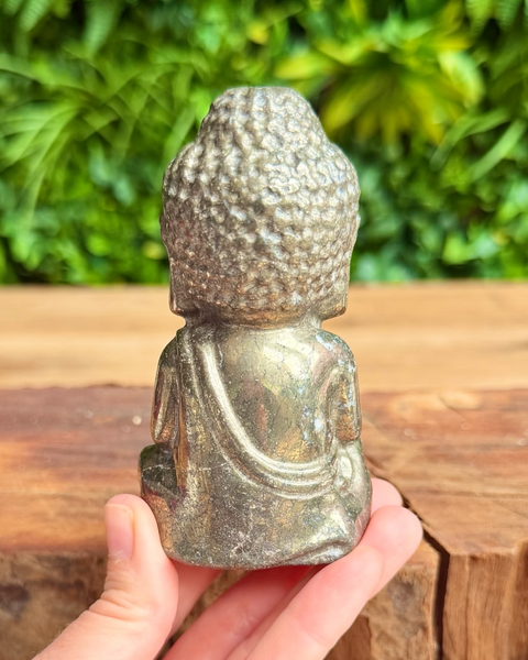Small pyrite  Buddha statue held in hand with greenery in the background