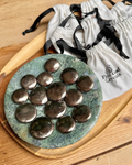 Round green stone tray with metallic stones on a wooden surface, with 'Feel good Crystals' bags in the background.