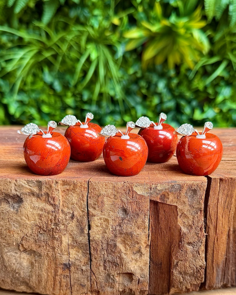 red jasper crystal apples with silver leaves on a wooden surface with green foliage in the background