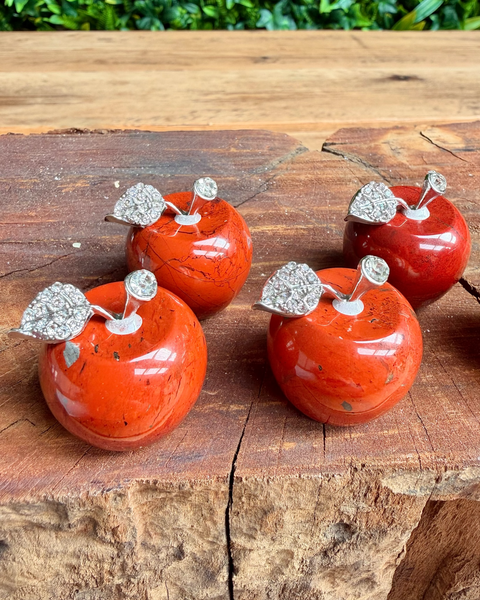 Four red jasper crystal apple-shaped  with silver leaves on a wooden surface