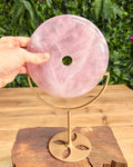 Rose quartz donut stone on a gold stand held by a hand with a natural background