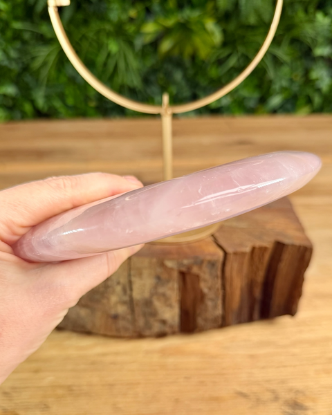 Hand holding a pink crystal on a wooden surface with greenery in the background