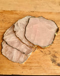 Three irregularly shaped rose quartz crystal slices with natural gold-colored edges, arranged on a light brown wooden surface.