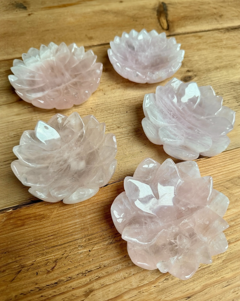 Five rose quartz crystal bowls on a wooden surface