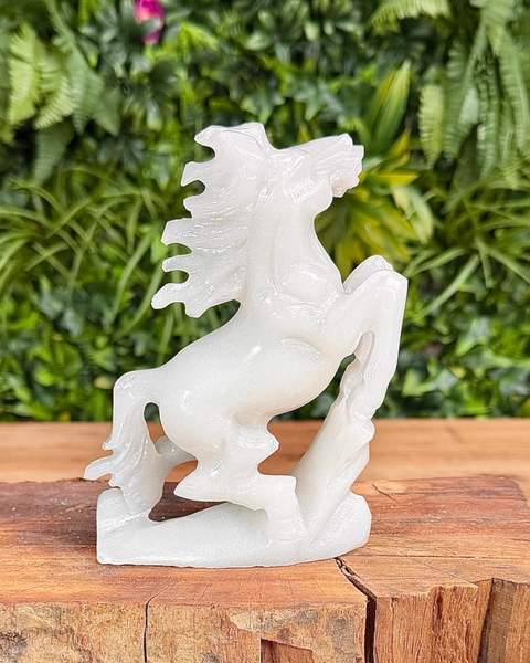 White jade horse sculpture on a wooden surface with green foliage in the background