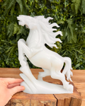 White jade horse statue on a wooden surface with a green leafy background