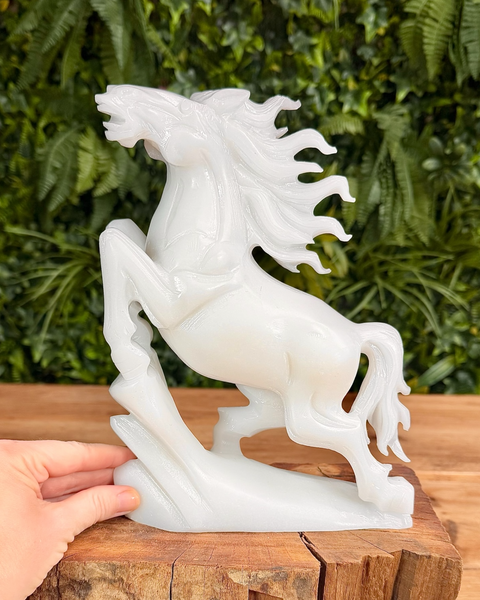 White jade horse statue on a wooden surface with a green leafy background