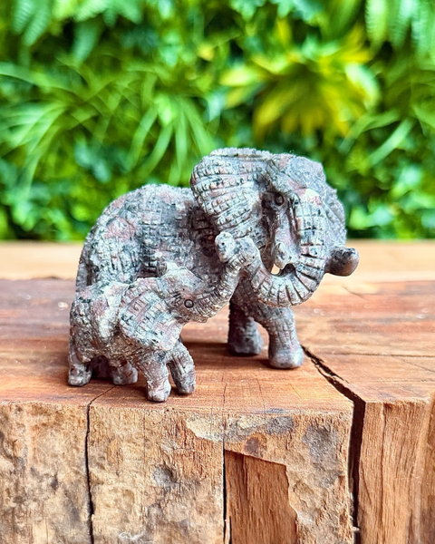 Two yooperlite  elephant sculptures on a wooden surface with green foliage in the background