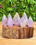 Set of six teardrop-shaped purple crystals on a wooden base with a green foliage background