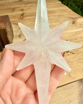 Clear star-shaped object held in a hand with a wooden surface in the background