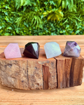 Four gem shaped crystal stones on a wooden block with a green leafy background