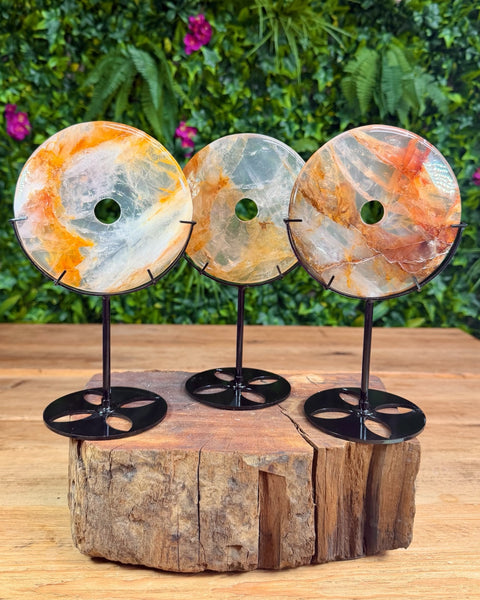 Three decorative stone discs on stands with a natural wood base and green foliage background