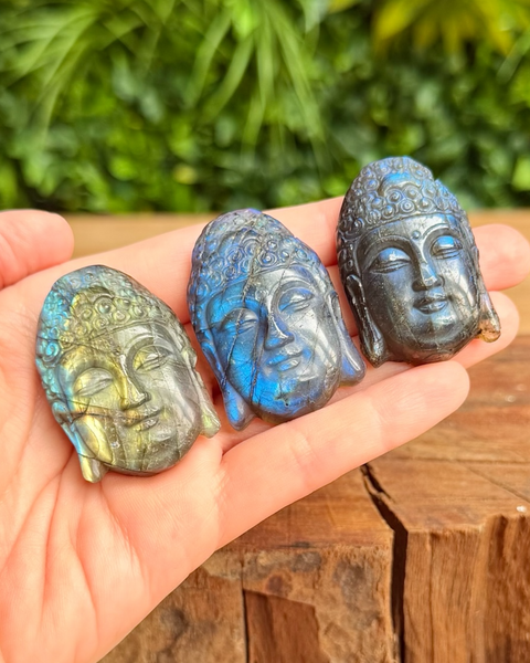 Three stone carvings of Buddha heads held in a hand with a natural background