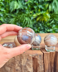 Person holding a polished moonstone sphere with more stones in the background on a wooden surface.
