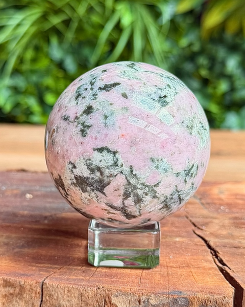 Polished multicolored stone sphere on a wooden surface with a natural background