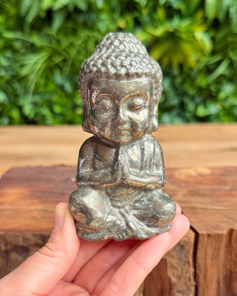 Small pyrite Buddha statue held in hand with greenery in the background