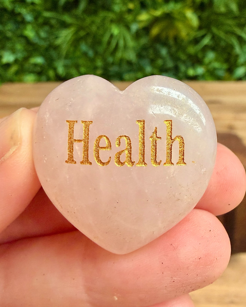Heart-shaped stone with 'Health' engraved on it held in a hand against a blurred green background