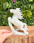White horse sculpture on a wooden block with a green leafy background